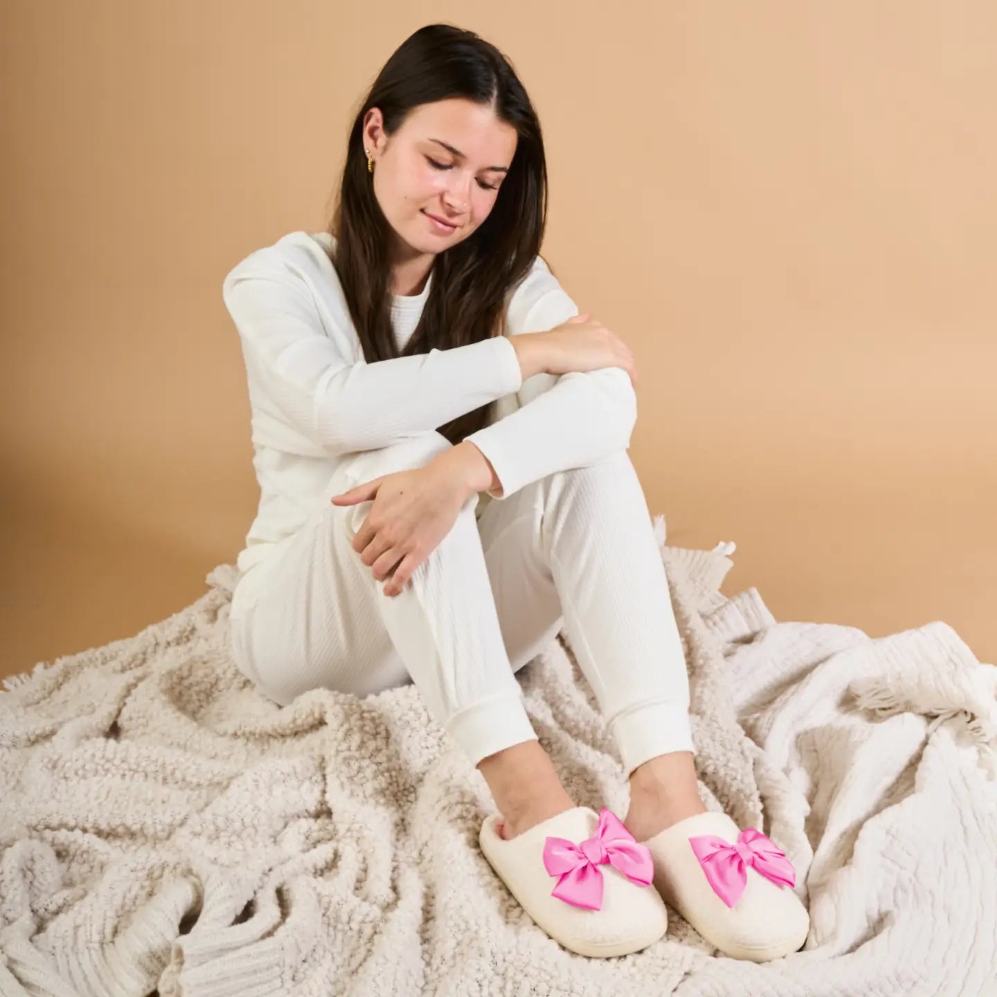 person wearing white pajamas and pink bow slippers on a beige background