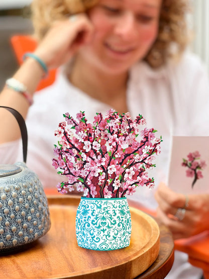 Cherry Blossom pop up bouquet set on a table with a person reading the enclosure card in the background.