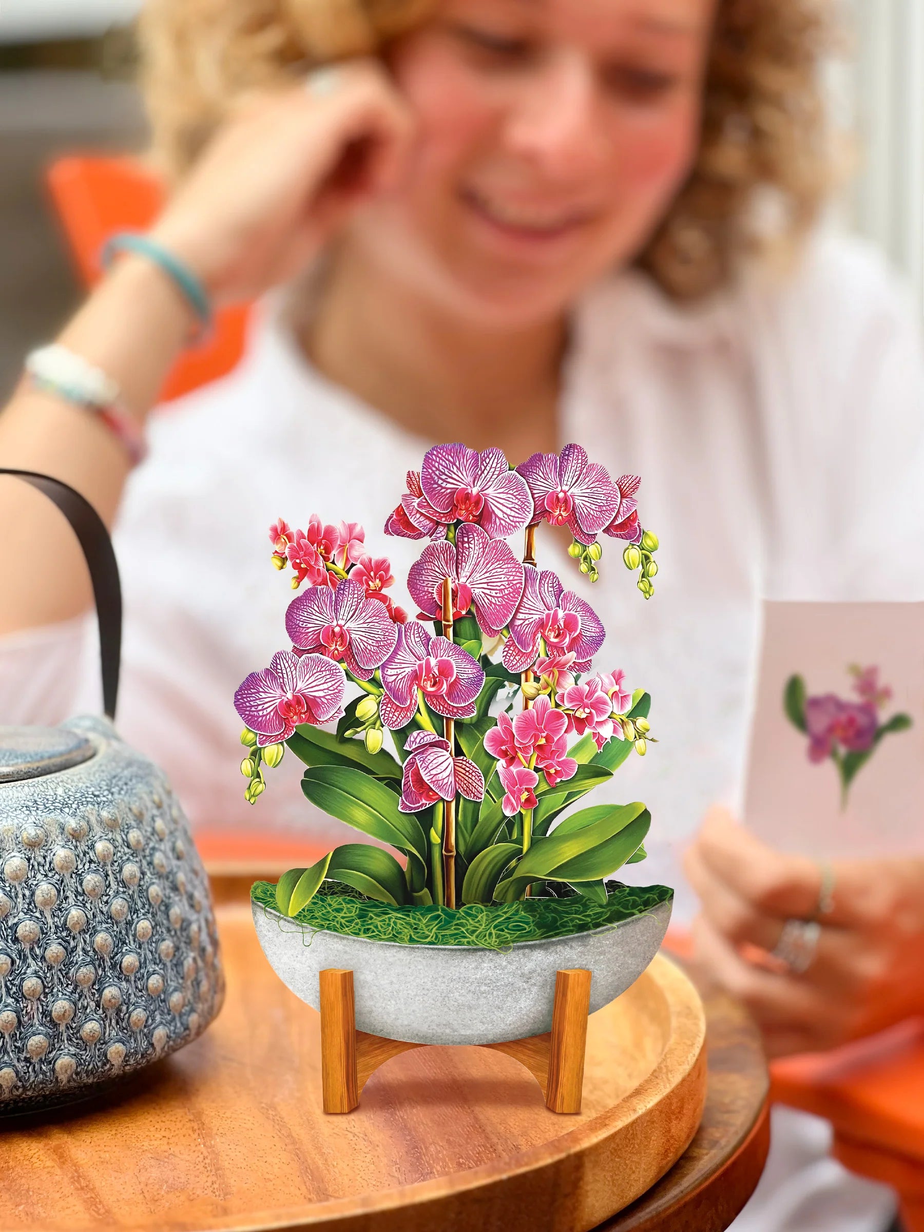 Orchid Oasis pop-up bouquet set on a table with person reading the enclosure card in the background.