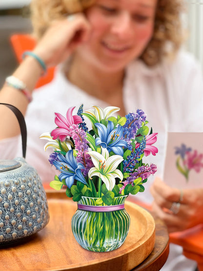 Lilies & Lupines pop-up bouquet set on a table with person reading the enclosure card in the background.