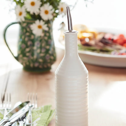 white ceramic oil bottle on a table with vase of flowers in the background