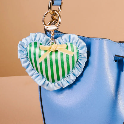 cool crush Heart-shaped bag charm with green and white stripes and a yellow bow attached to a blue bag.