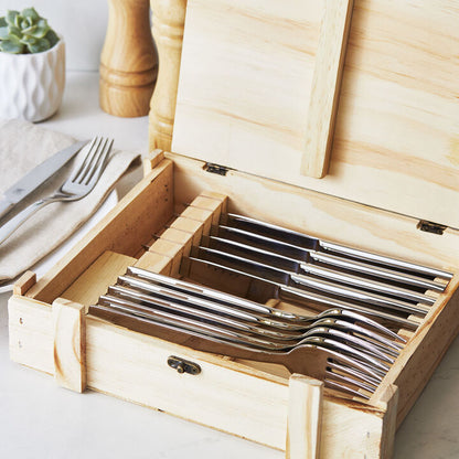 steak knife and fork set in open wooden box on a table with plates, napkins, and salt and pepper grinders in the background.