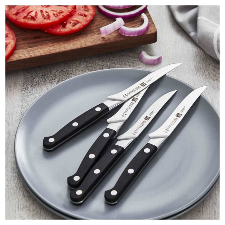 4 PRO Steak Knifes laying on a plate on a table with sliced tomatoes on a cutting board.
