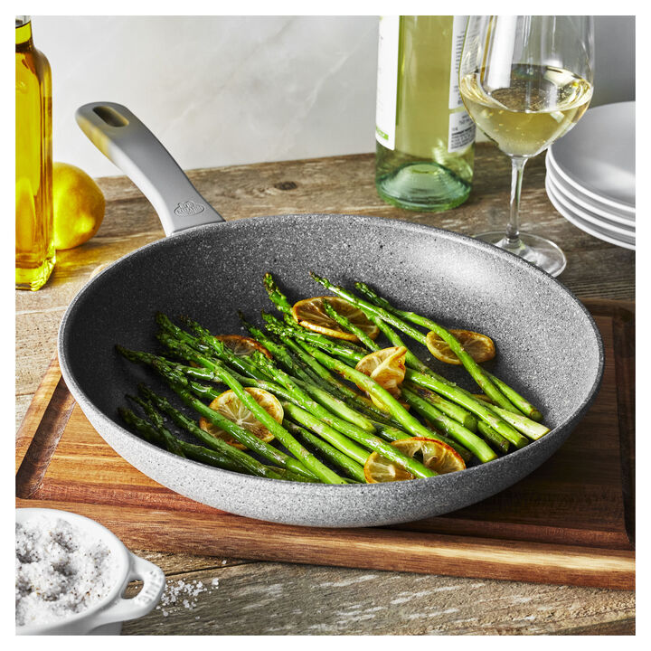 fry pan filled with asparagus and seasoning set on a wooden board on a countertop with wine and seasonings around it.
