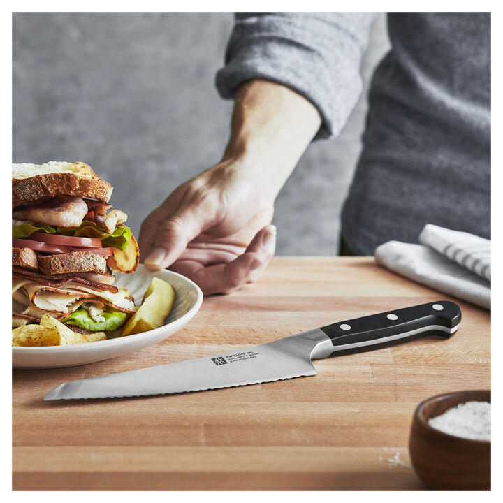 Pro 7 Inch Bread Knife laying on a wood board and a hand reaching for a plate of prepared food.