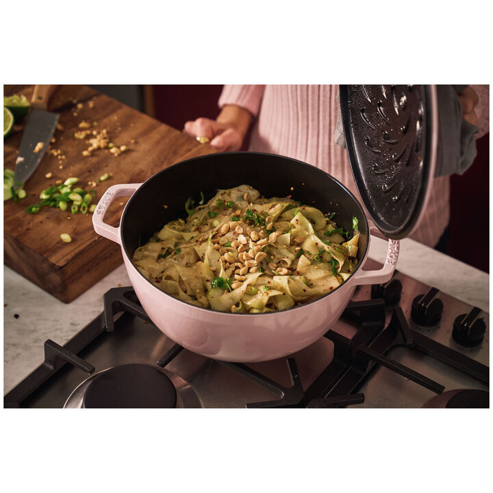 Sorbet rose French oven set on a stove top with a person holding the lid up showing cooked food inside