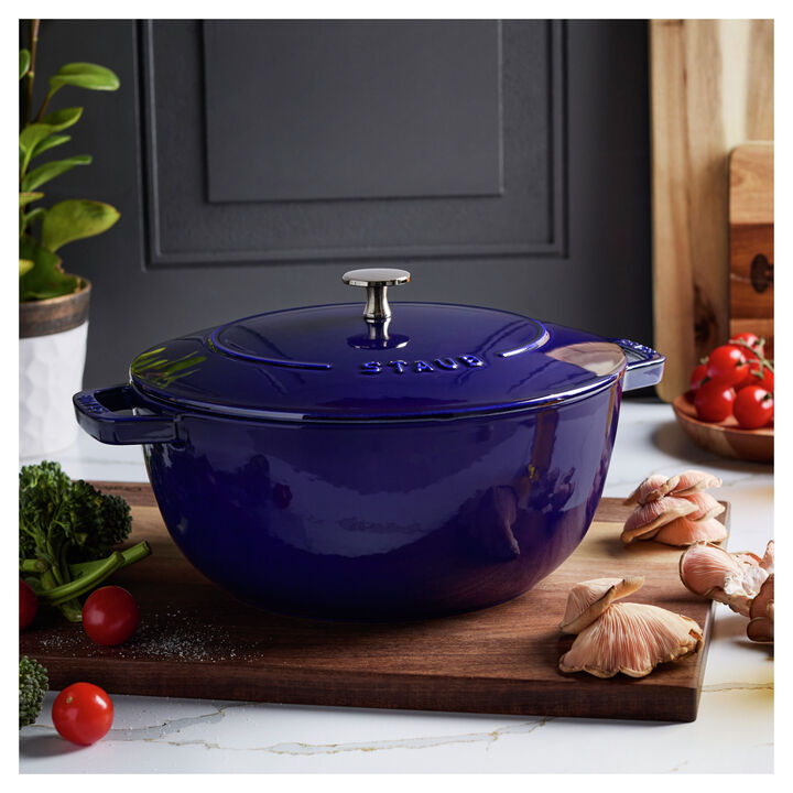 Dark blue French oven set on a wooden board on a kitchen counter top surrounded by veggies