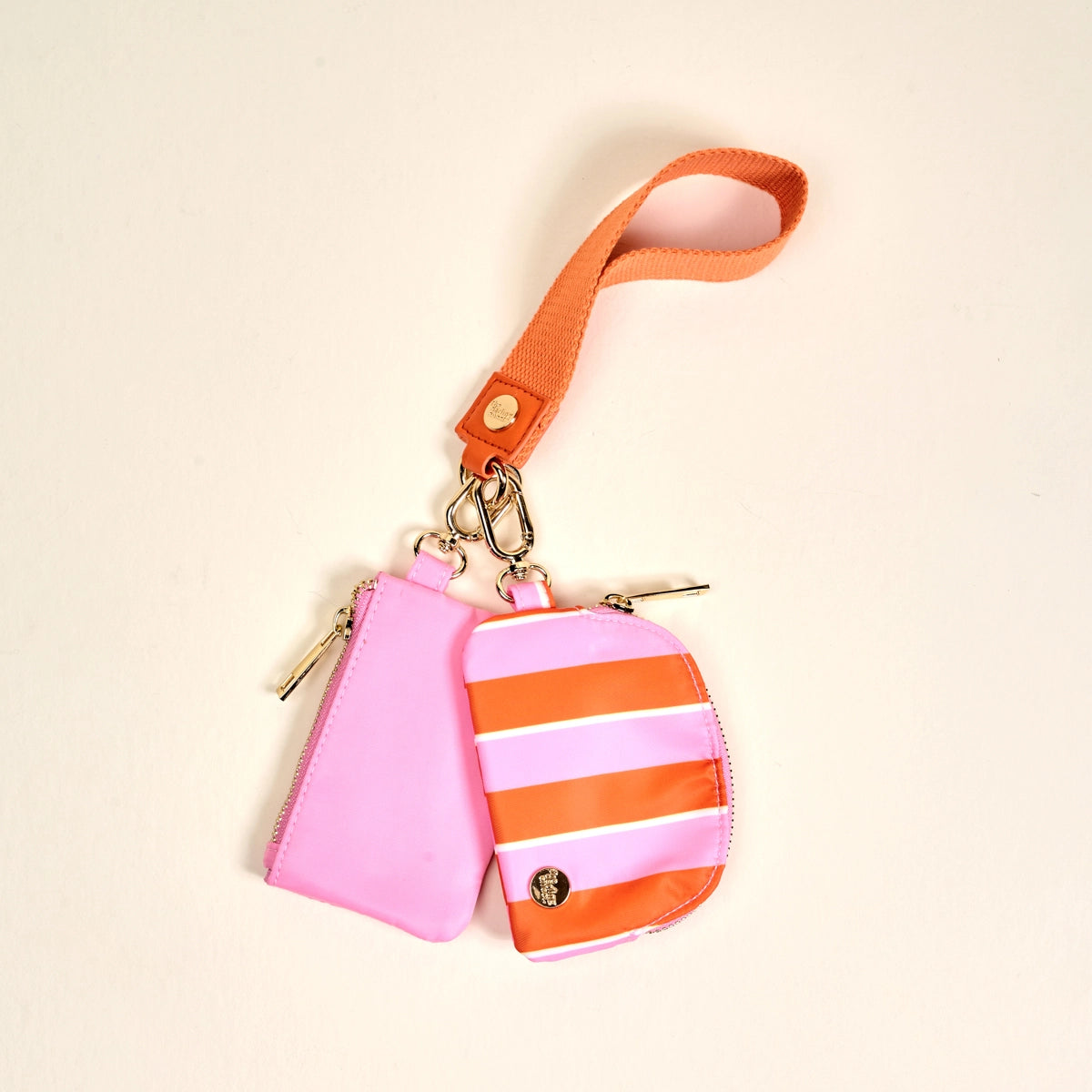 Pink and orange striped keychain pouch with wrist strap on a beige background