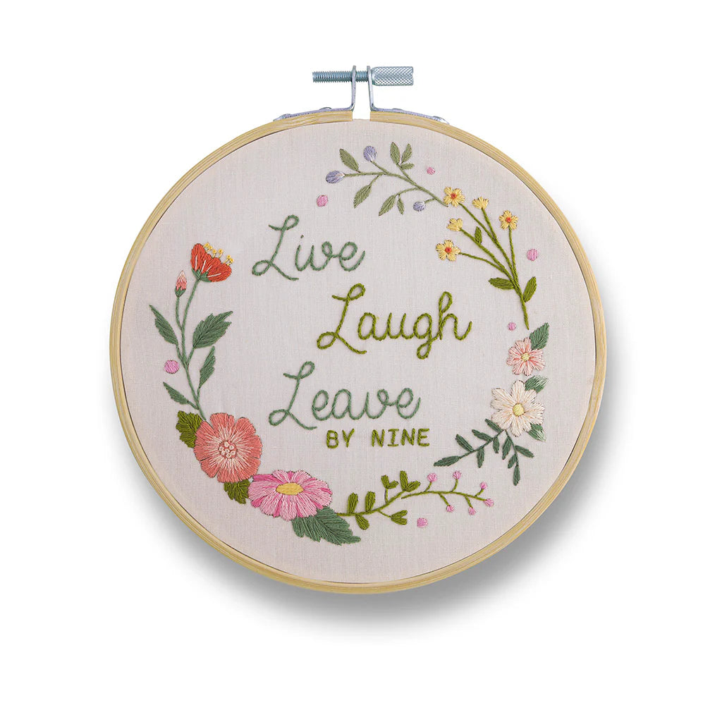 Embroidery hoop with floral design and text 'Live Laugh Leave by Nine' on a white background