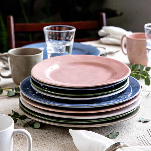 stack of juliska puro dinner and salad plates in assorted colors on a table with glasses and mugs.