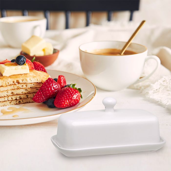 White butter dish on a table with pancakes, berries, and coffee.
