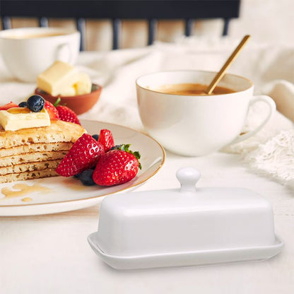 White butter dish on a table with pancakes, berries, and coffee.