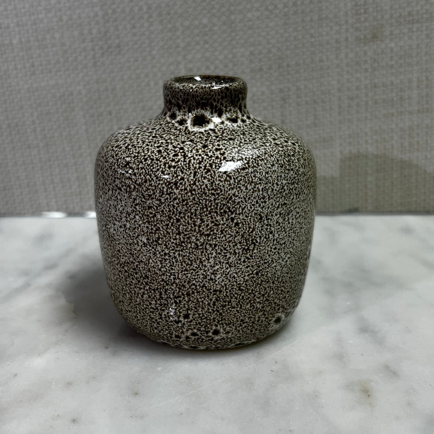 short ivory vase with brown speckled design.