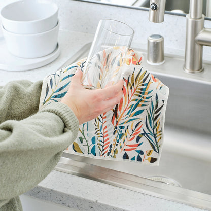 Hand using all purpose colorful leaves towel to clean a glass in the kitchen sink.