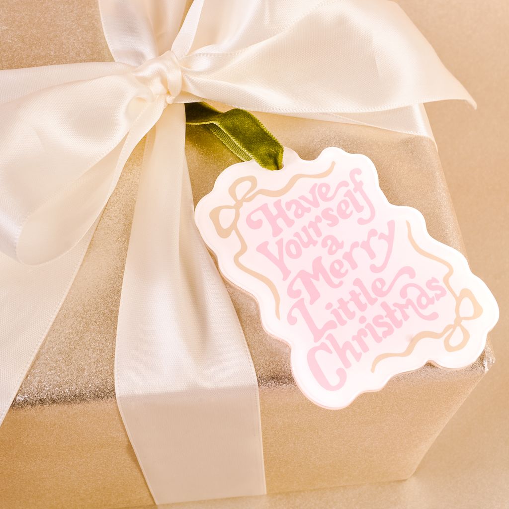 white flat acrylic ornament with pink text that says "have your self a merry little Christmas" tied on a package