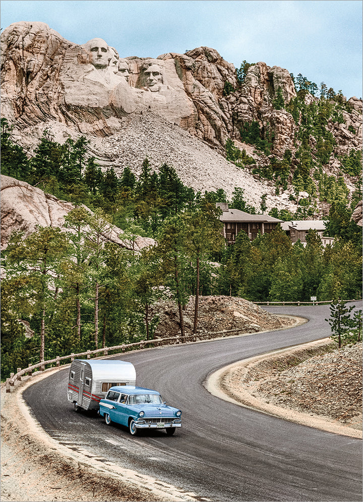 photo of a car pulling a camper down the road in front of mt. rushmore