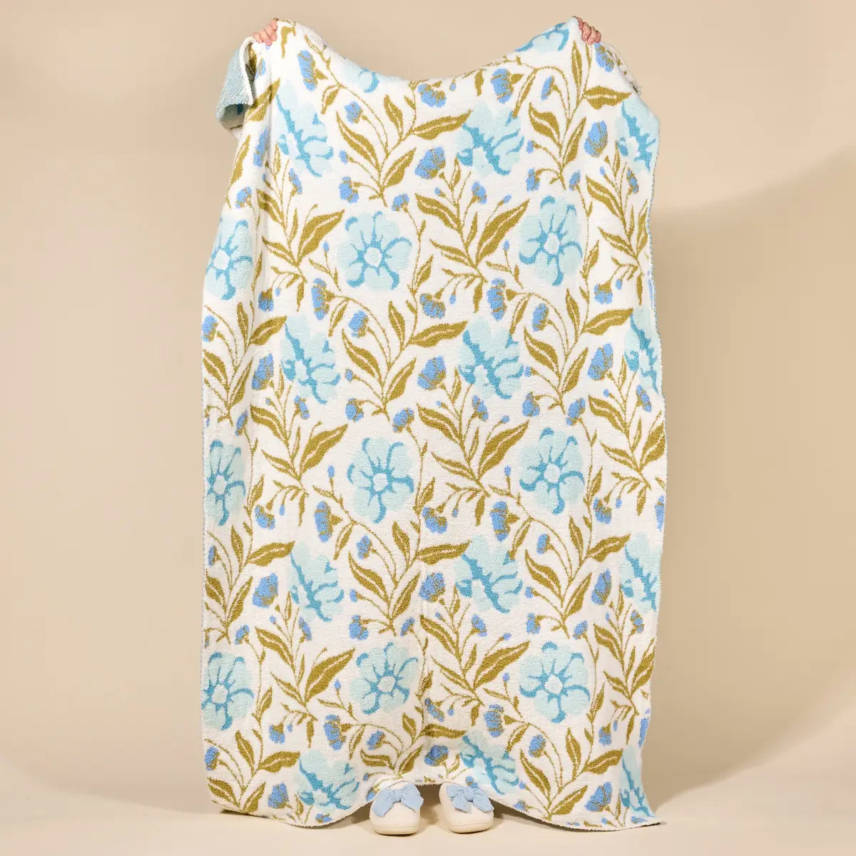 Floral patterned blanket being held up from behind on a beige background