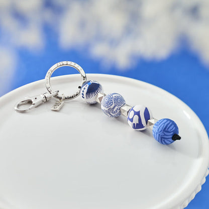 Santorini Four-Ball Keychain laying on a dish with a sky background