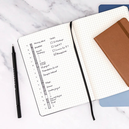 Open notebook with grid pages and a pen on a marble surface
