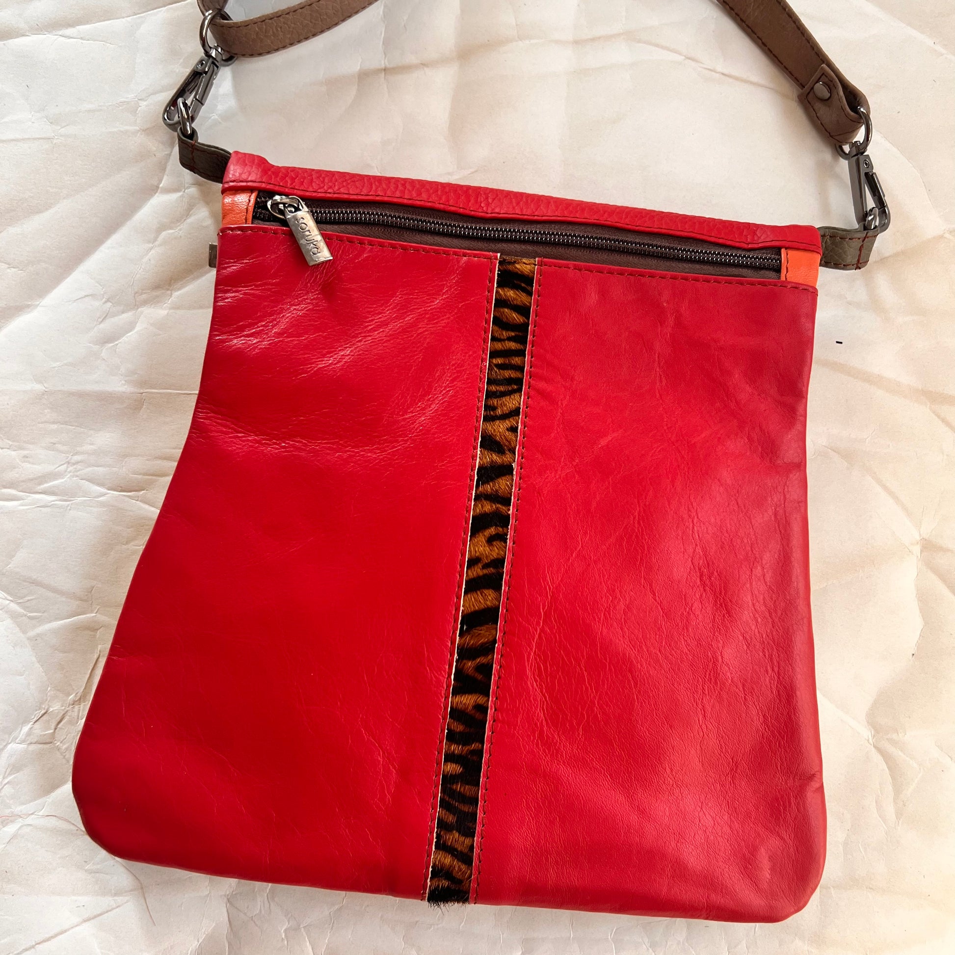 red greta bag with animal print stripe downt he center and zipper across the top.