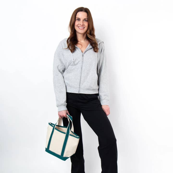 a person wearing black pants and grey hoodie holding off white tote with teal green handles and trim