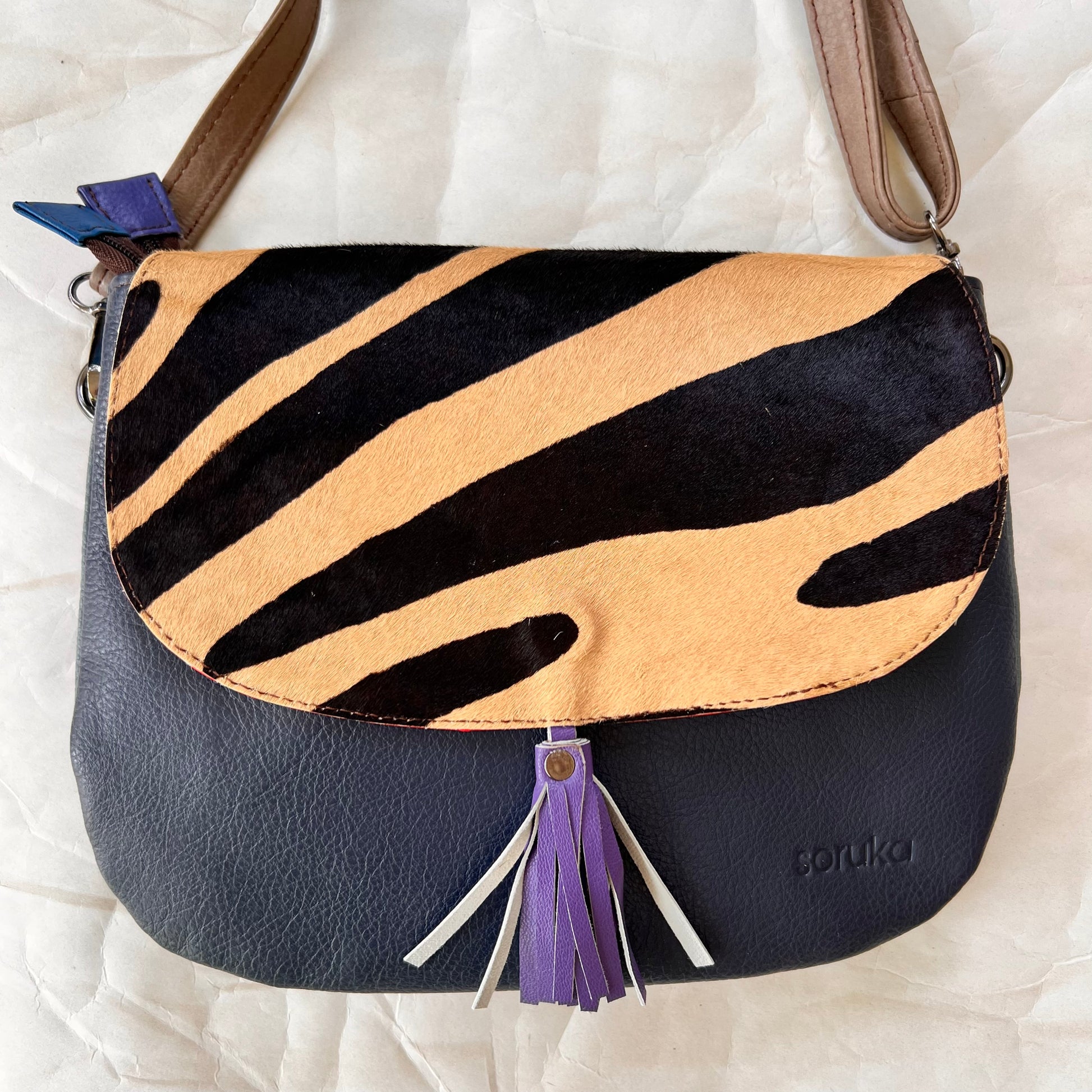 lola bag with animal print hair-on-hide flap with purple tassel over a navy body.