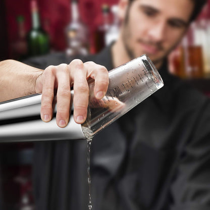 person standing behind a bar using double wall boston shaker to prepare and pour a drink.