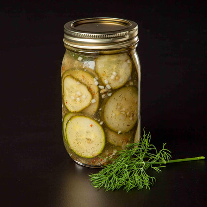 jar filled with pickled cucumbers with a sprig of dill next to it.