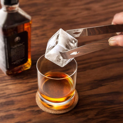 glass filled with with beverage and a hand holding tongs dropping a large ice cube in to it.