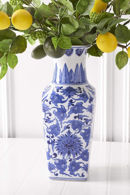 white vase with blue floral design filled with branches of lemons and limes.