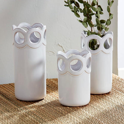 all three sizes of the scalloped bud vases displayed on a tan runner with one having dried greenery