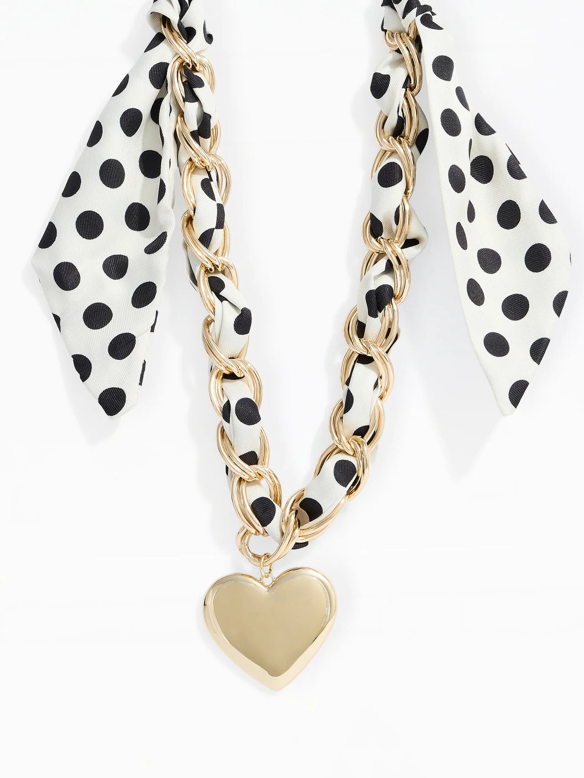 A gold chain necklace with a heart-shaped pendant, featuring a white silk scarf with black polka dots woven through the chain, set against a plain white background.