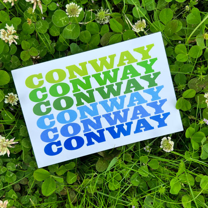 white postcard with "conway" printed 6 times in greens and blues laying in a field of clovers.