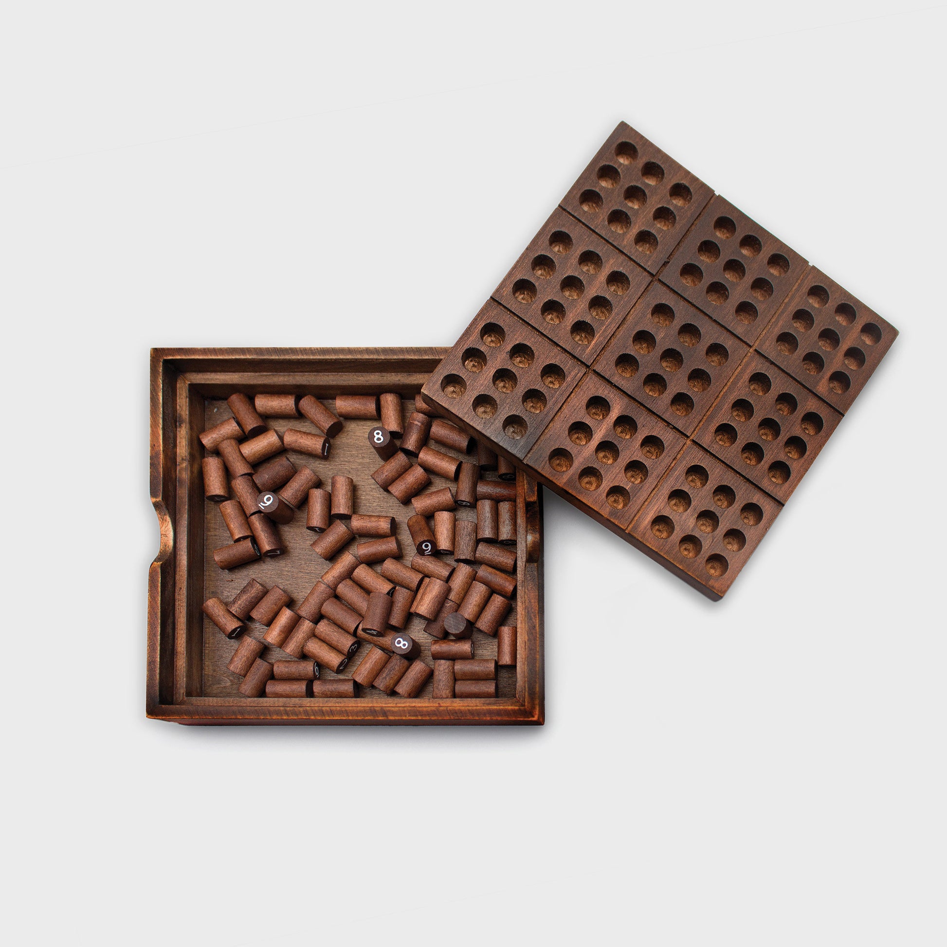 Wooden Sudoku game with lid set to side and numbered pegs in the storage box.