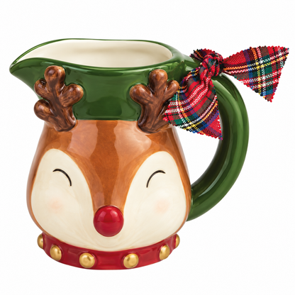 A ceramic holiday pitcher bud vase shaped like a reindeer face, with brown antlers on a green hat, a red nose, and a red plaid bow on the handle, shown on a white background.