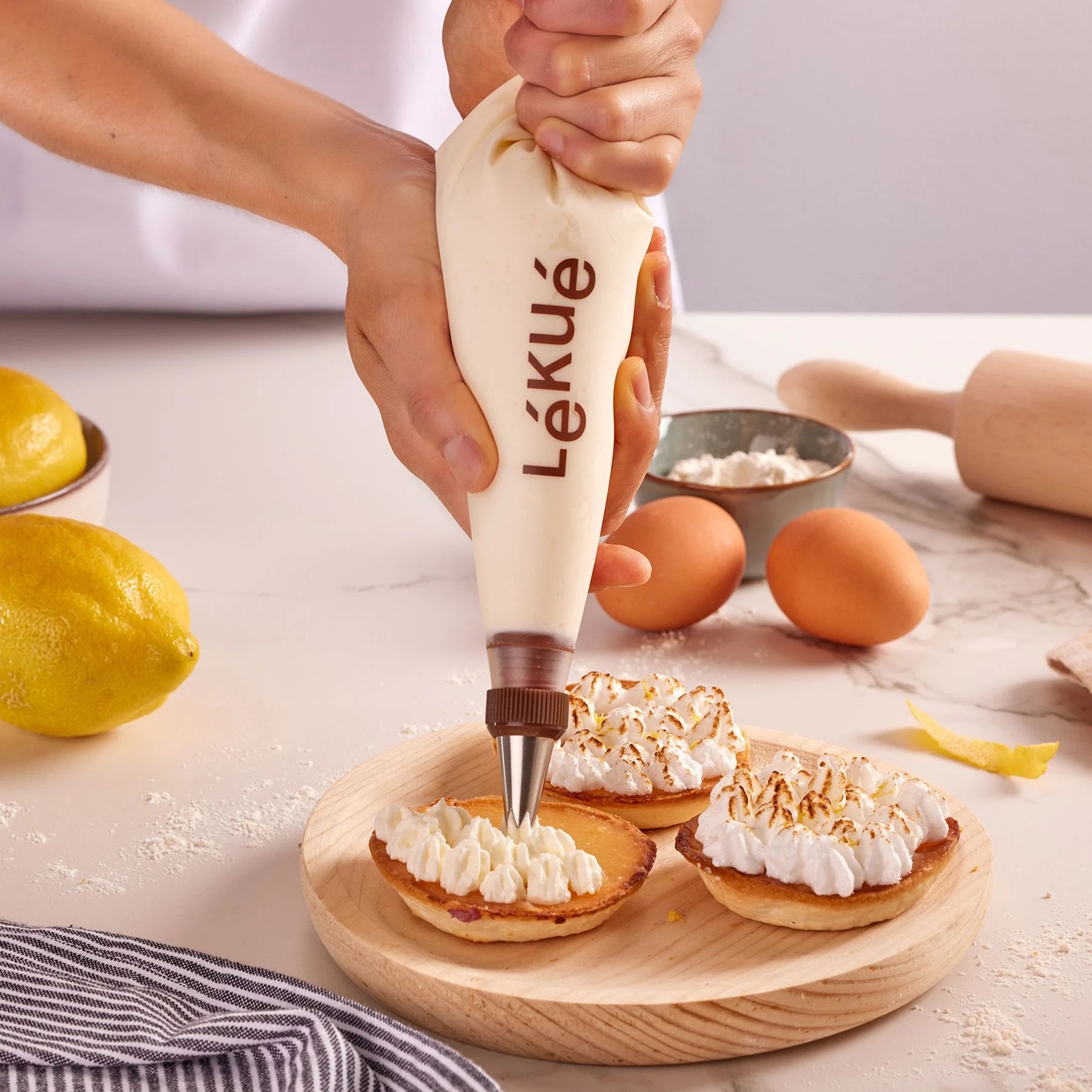 Person using a Lékué piping bag to fill small pastries with cream on a kitchen counter.