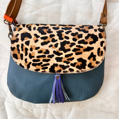 lola bag with cheetah print hair-on-hide flap with royal tassel over a teal body.
