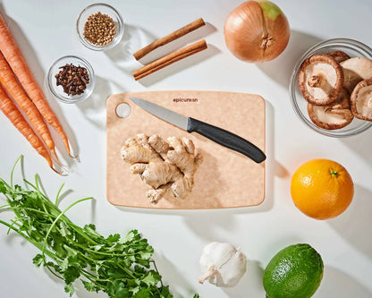 small natural epicurean cutting board with a knife on it on a countertop with fruit, veggies, and spices.