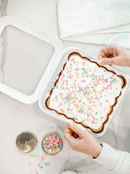 top view of a hands putting a foil pan filled with cake in to a white fancy panz.