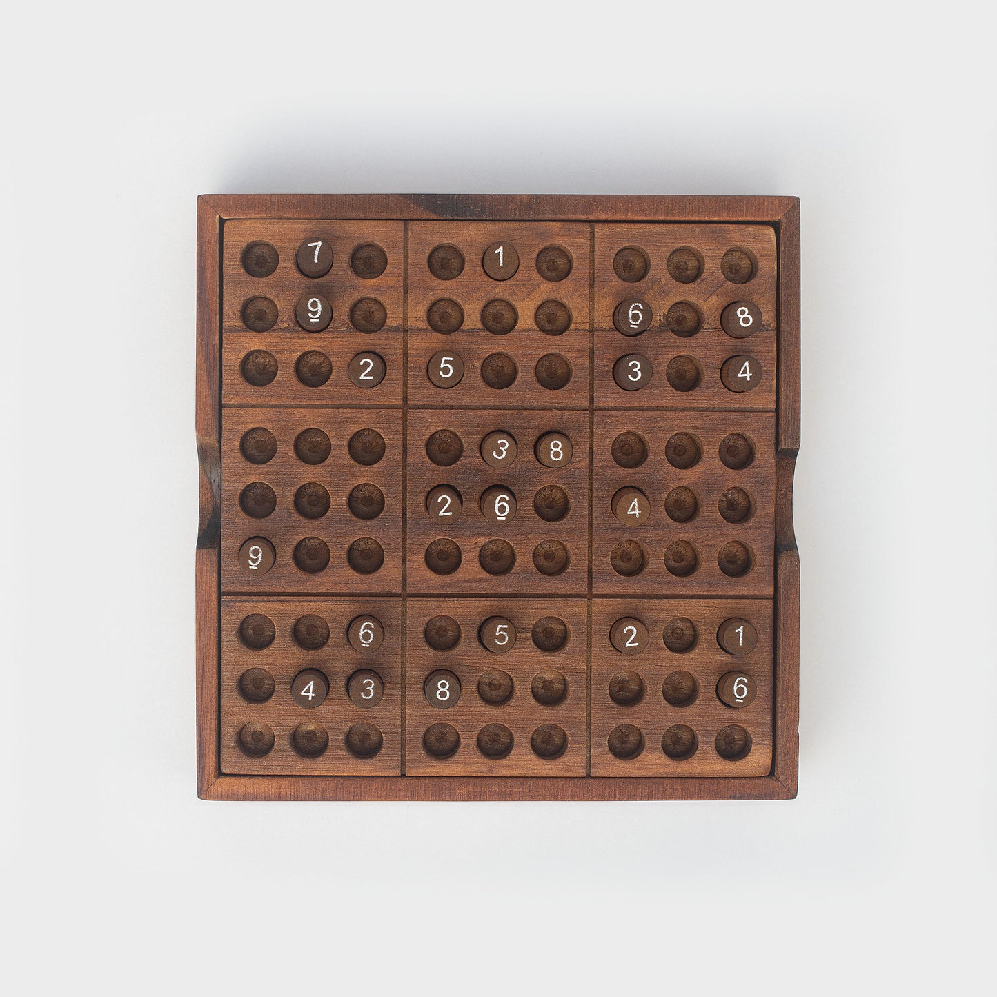 Top view of wooden Sudoku game with some numbered pegs in slots.