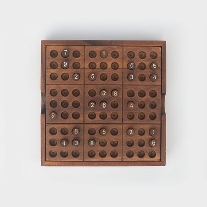 Top view of wooden Sudoku game with some numbered pegs in slots.