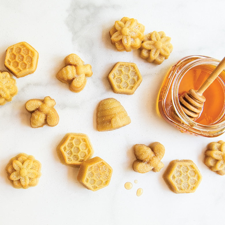 busy bee bitelets in the shapes of flowers, bees, beehives, displayed on a white surface next to a jar of honey