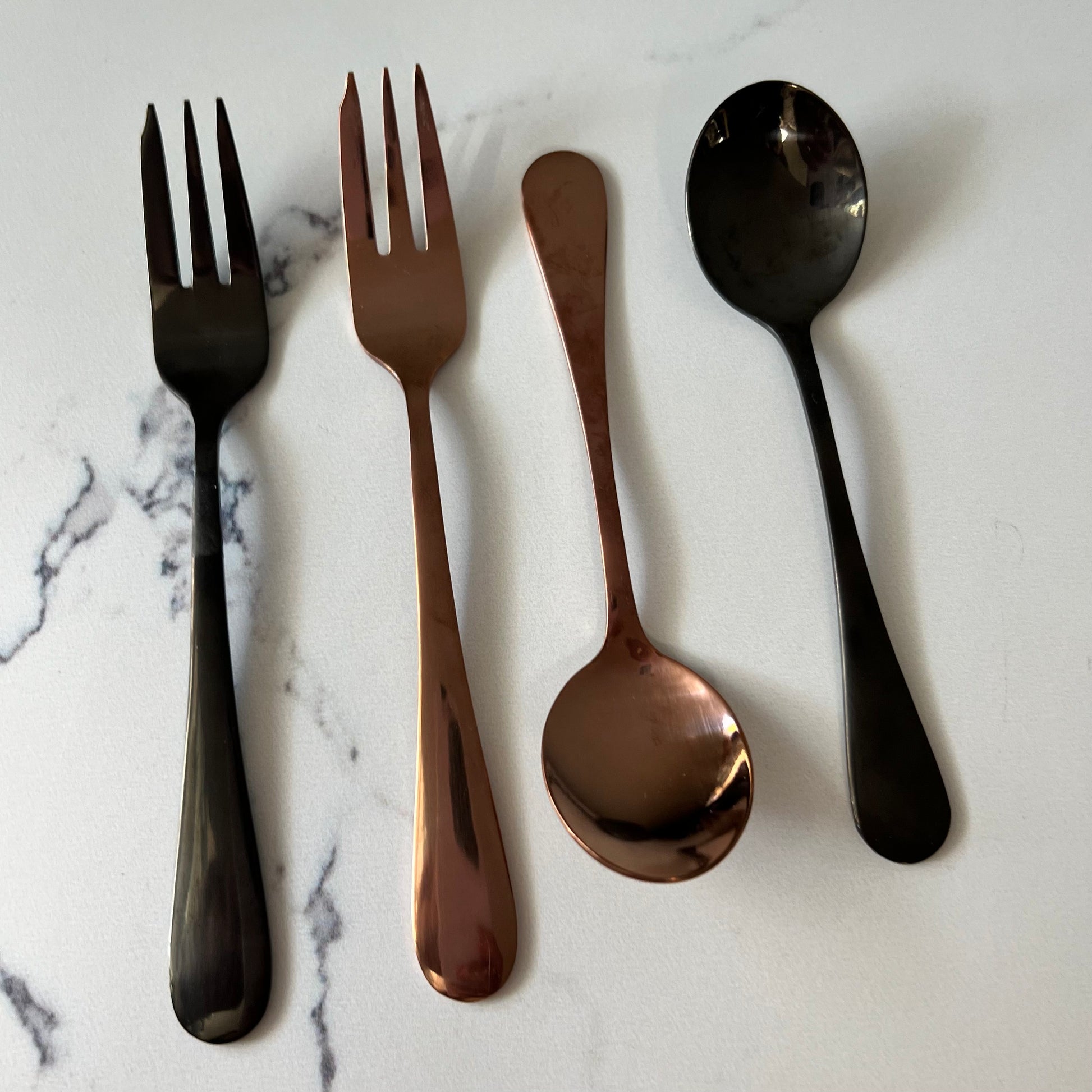 2 forks and 2 spoons arranged on a marble countertop.