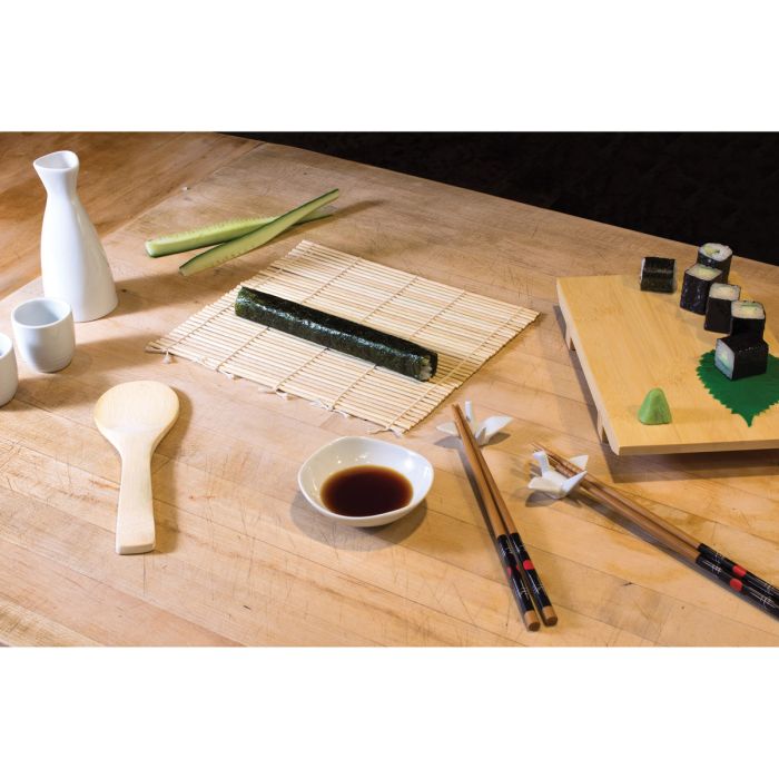 Sushi preparation setup on a wooden table with sushi rolls, soy sauce, and chopsticks.