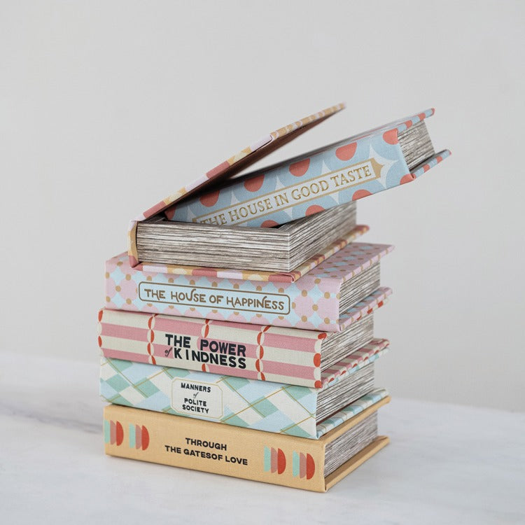 Stack of books with decorative covers on a light background, top book box is open showing storage inside