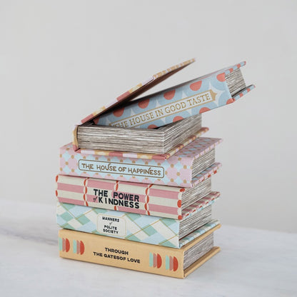 Stack of books with decorative covers on a light background, top book box is open showing storage inside