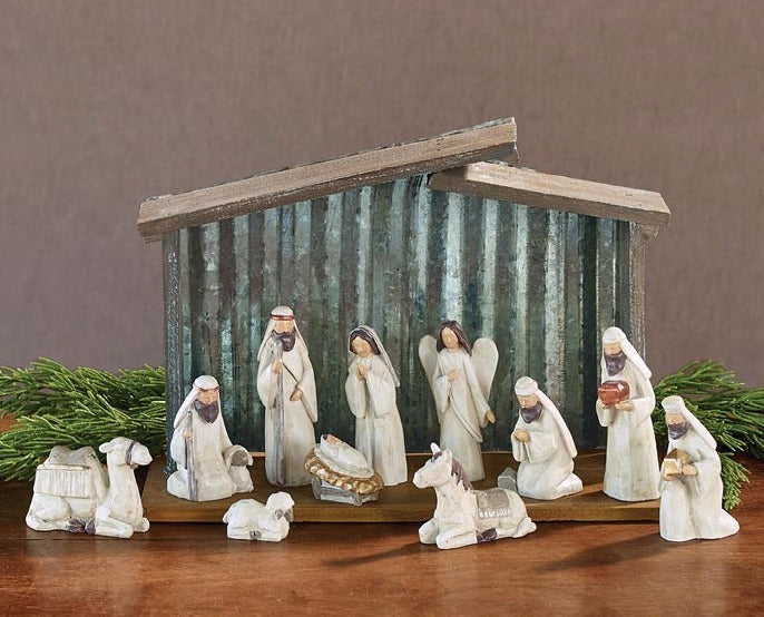 blessed beginnings nativity set displayed with tin creche on a wooden table with pine sprigs behind it