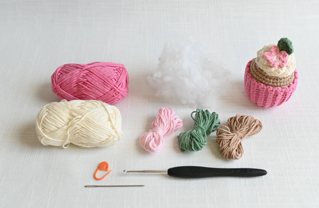 Parts of a crochet kit for crocheting a cupcake arranged on a white background.