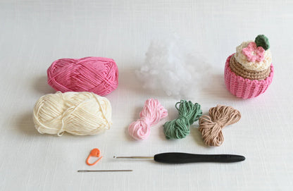 Parts of a crochet kit for crocheting a cupcake arranged on a white background.